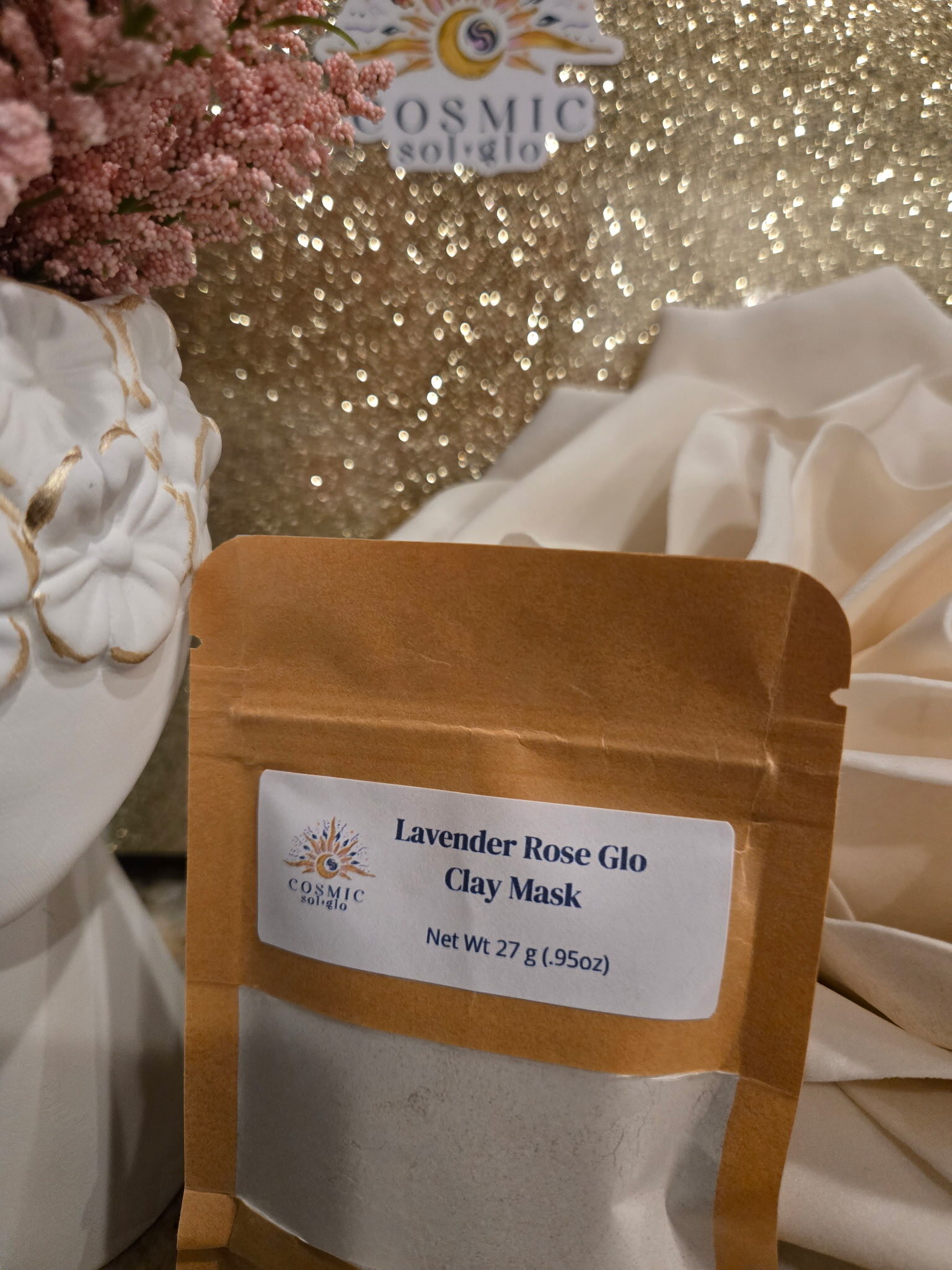 Lavender Rose Glo clay mask pouch styled with pink flowers, a Cosmic Sol Glo sticker, and gold glitter