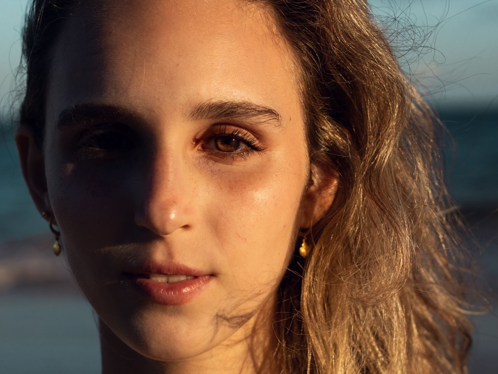 A woman in warm golden-hour light with the coast softly visible behind her