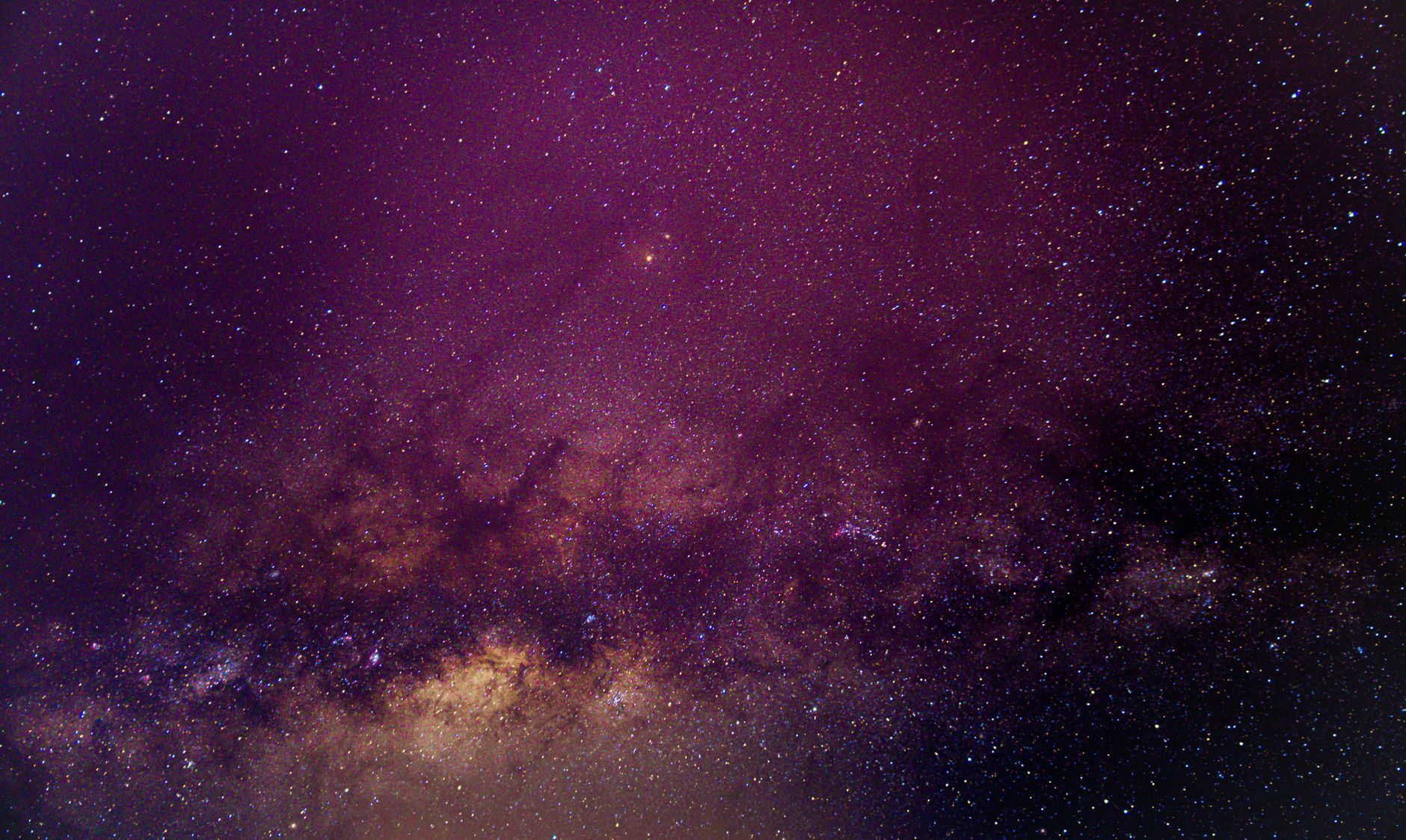 The Milky Way with a warm golden core arcing across a deep purple night sky