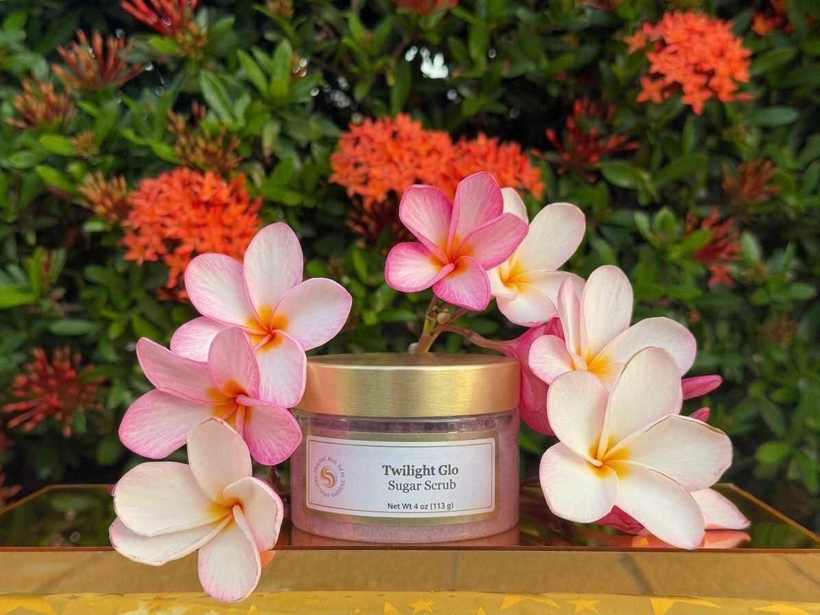 Twilight Glo lavender sugar scrub jar with plumeria against green foliage