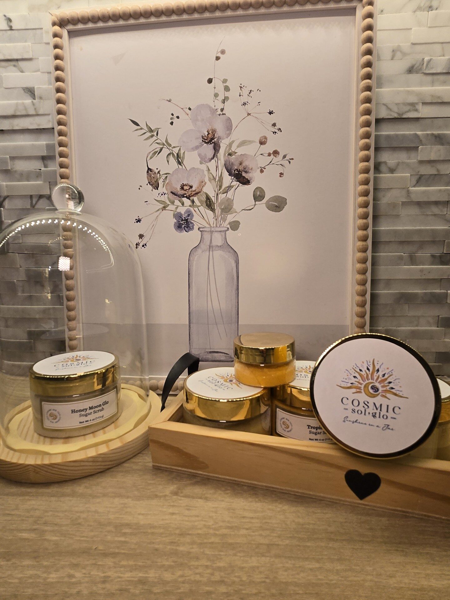 Cosmic Sol Glo jars styled on a wooden vanity tray with a glass cloche and floral art