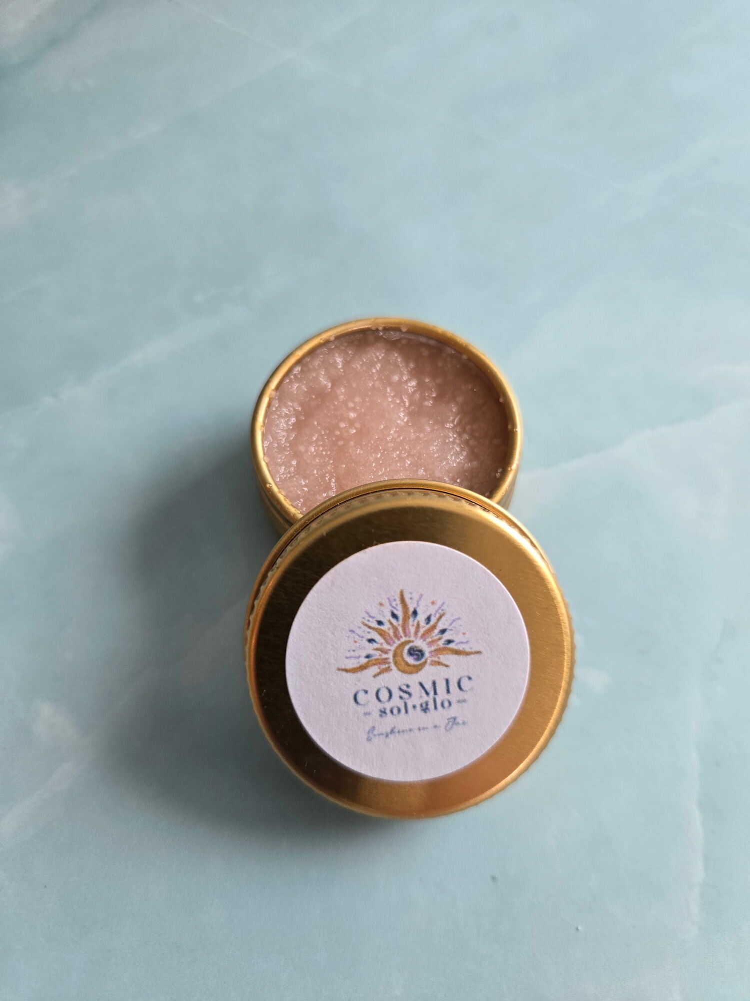 Cosmic Sol Glo Galaxy Pop lip scrub, a pink bubblegum-scented scrub in an open gold tin