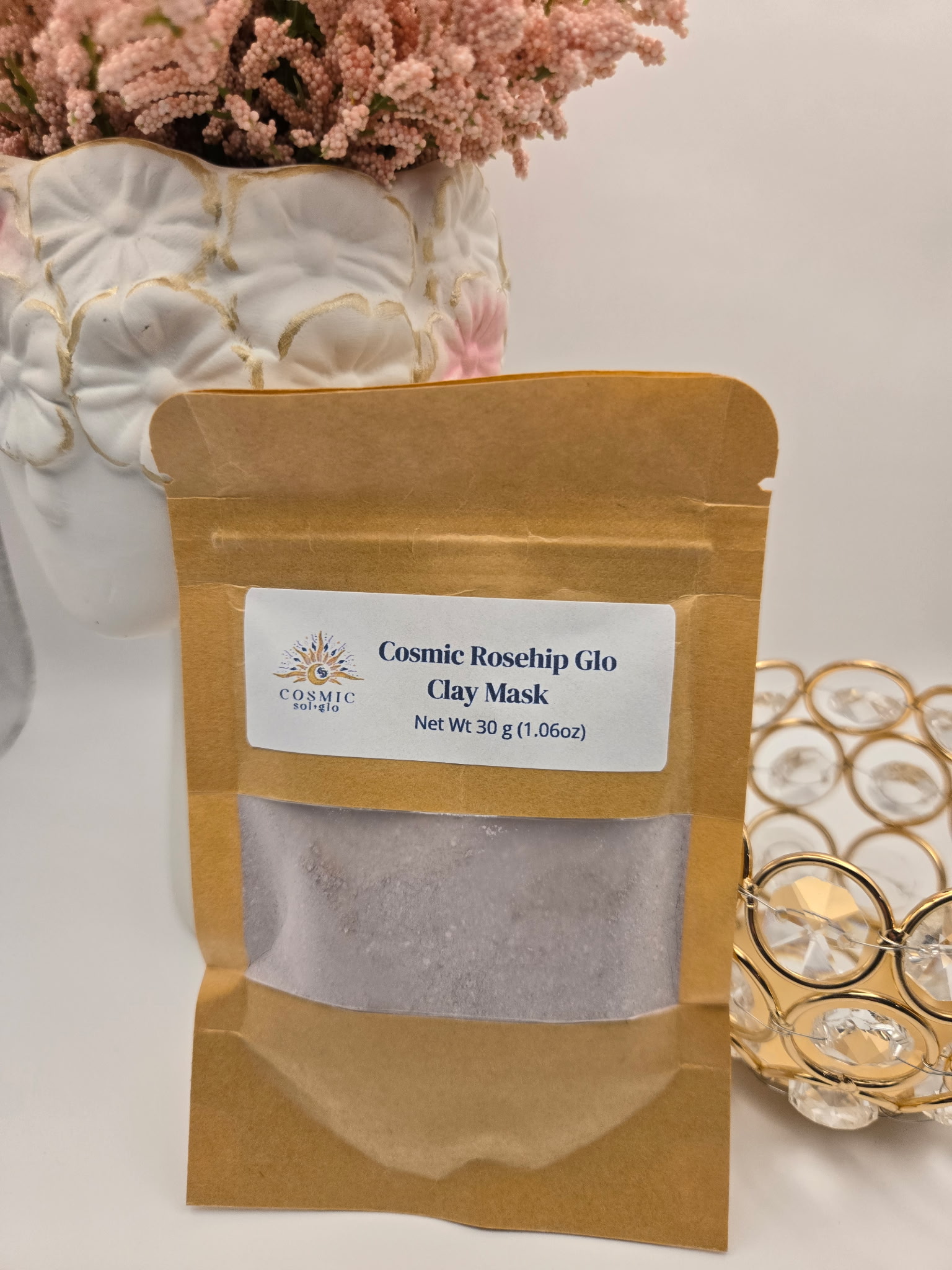 Cosmic Rosehip Glo Clay Mask pouch styled with dried pink flowers in a white vase